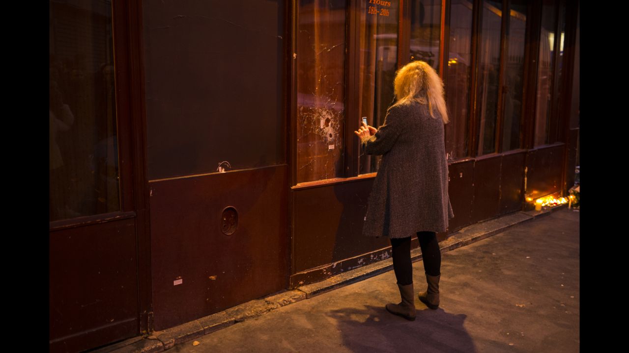 A woman takes a picture of a window shattered by bullets on November 14.