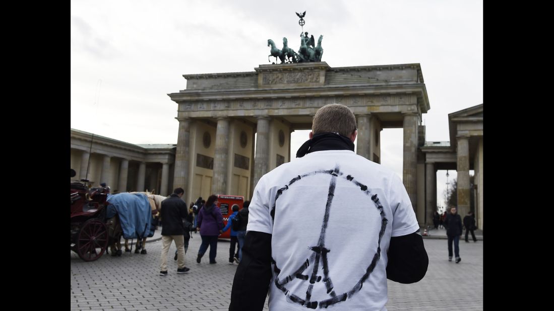 A man wears a shirt with a sign combining a peace symbol with the Eiffel tower in front of the Brandenburg Gate near the French embassy in Berlin.