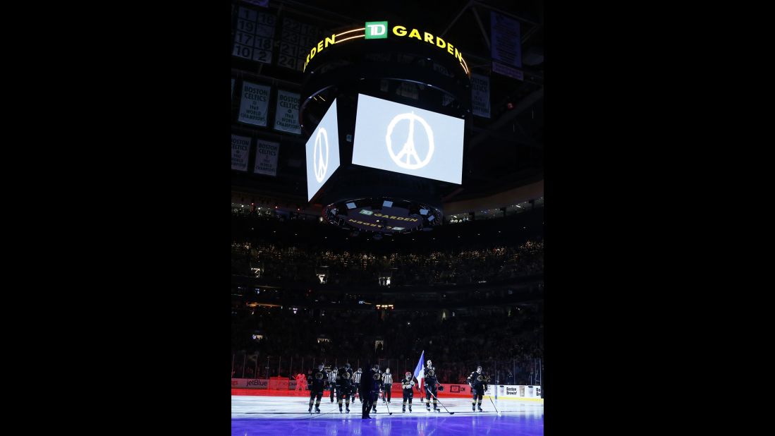 The Boston Bruins and the Detroit Red Wings stand on the ice while the French national anthem is played before an NHL hockey game in Boston. The symbol for 'Peace for Paris' appears above the rink.