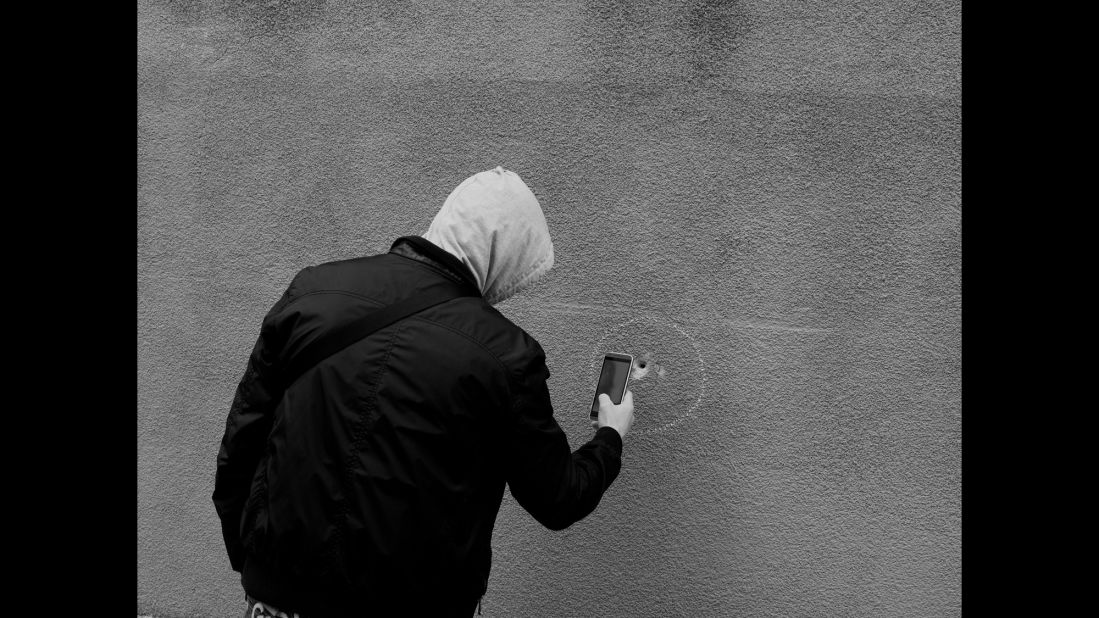A man uses his phone to take a photo of a bullet hole near Le Carillon and Le Petit Cambodge. The photographer says he tries to capture the theatrical side of life, using light in a way that "creates this idea of fiction, of theater."<br />