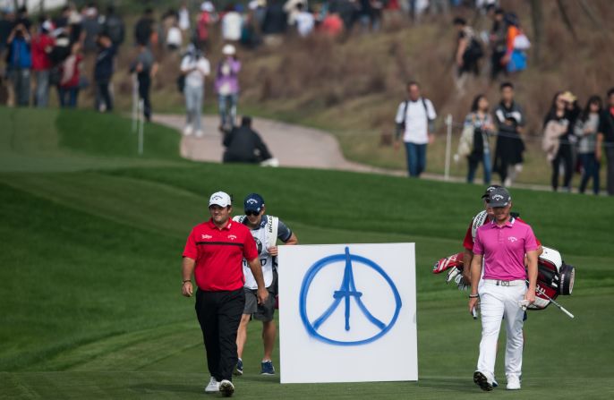 Patrick Reed (L) of the US and Kristoffer Broberg (R) of Sweden pass a sign placed to commemorate the victims of the Paris attacks during the Shanghai Masters.