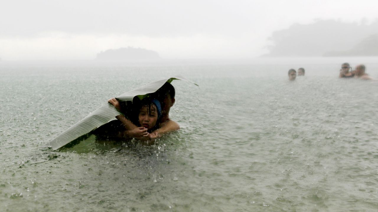 <strong>October 17:</strong> A man and girl use a banana leaf to cover themselves from the rain as they wade in the sea on the outskirts of Colon, Panama.