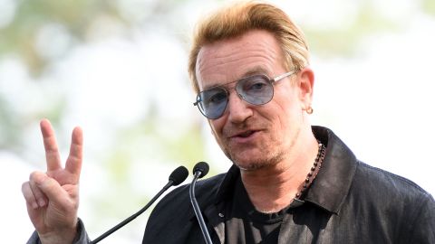 Bono holds up a peace sign during a dedication ceremony for a giant tapestry, from Amnesty International, in honor of John Lennon on Ellis Island July 29, 2015, in New York. 