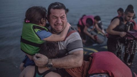 <strong>August 15:</strong> A refugee, holding his son and daughter, cries tears of joy after their boat arrived on the Greek island of Kos. The island in the Aegean Sea has been overwhelmed by refugees.