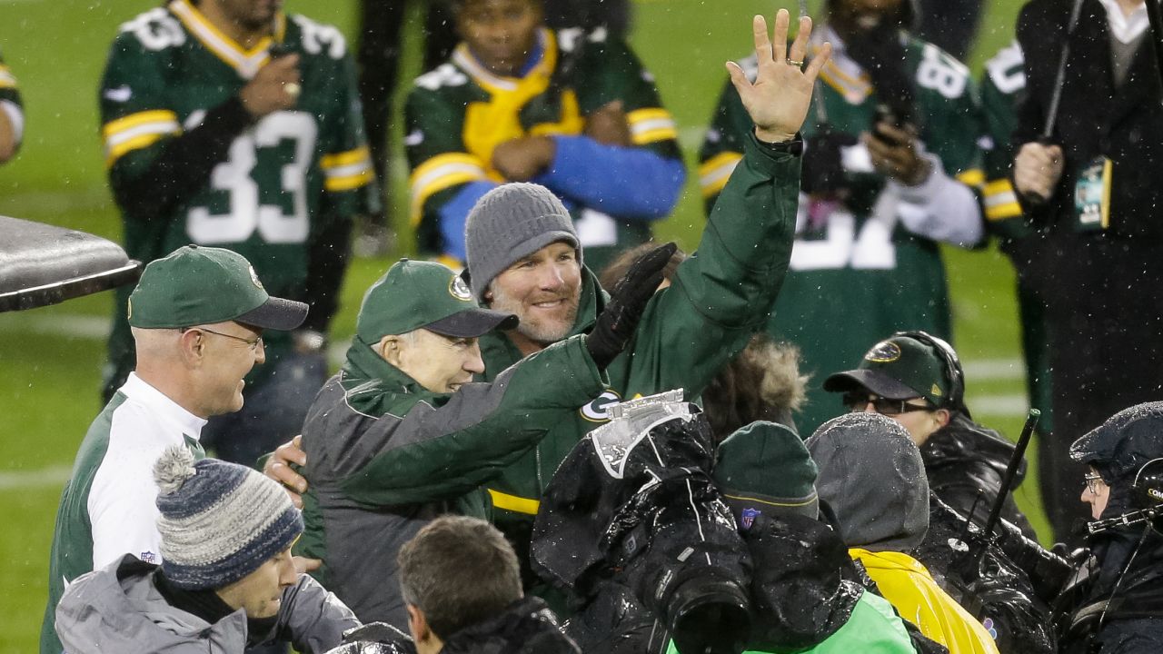 Former NFL quarterback Brett Favre, wearing the knit cap, waves to the crowd in Green Bay, Wisconsin, during his jersey retirement ceremony on Thursday, November 26. Waving with Favre is fellow Packers great Bart Starr. 