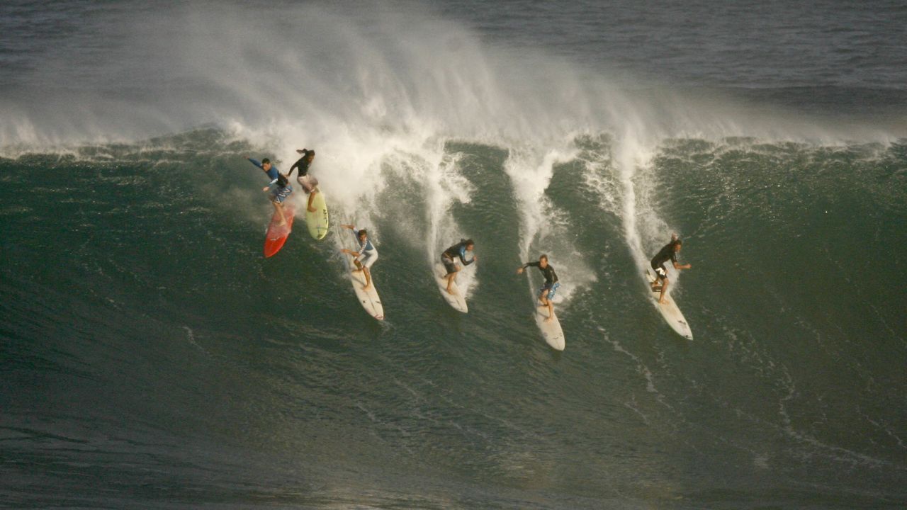 Six surfers drop into a wave during pre-contest surfing at the Eddie Aikau Big-Wave Invitational in 2009.
