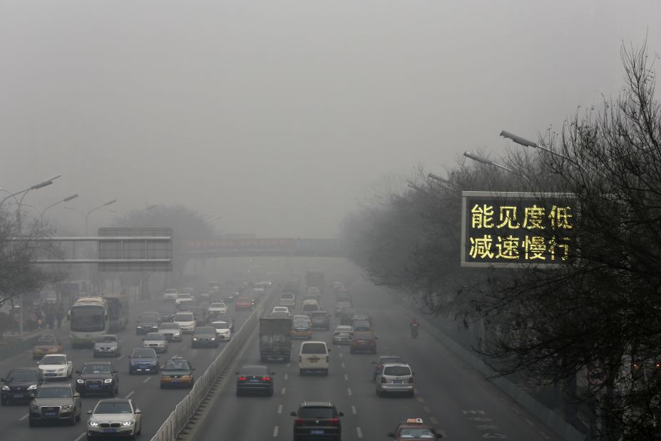 Vehicles drive along a highway in Beijing with a traffic sign that reads "Slow down, low visibility" on November 30.
