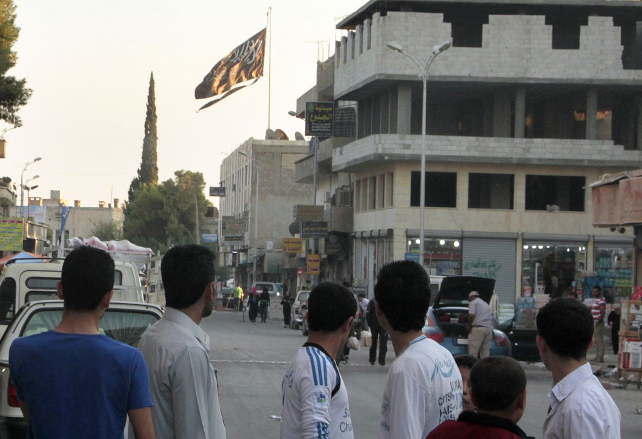 Men look at a large black jihadist flag in Raqqa on September 28, 2013. In Raqqa today, school is banned -- and even small pleasures, like chocolate, are an unaffordable luxury because many cannot work.