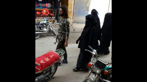 In this photo from November 6, 2015, an ISIS fighter walks along a street in Raqqa with his 3 wives walking behind him, according to RBSS.