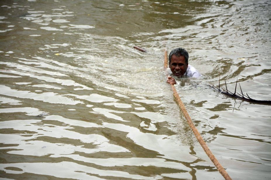 An Indian man clings to a rope as he makes his way through flood waters in Chennai on December 2,aid.