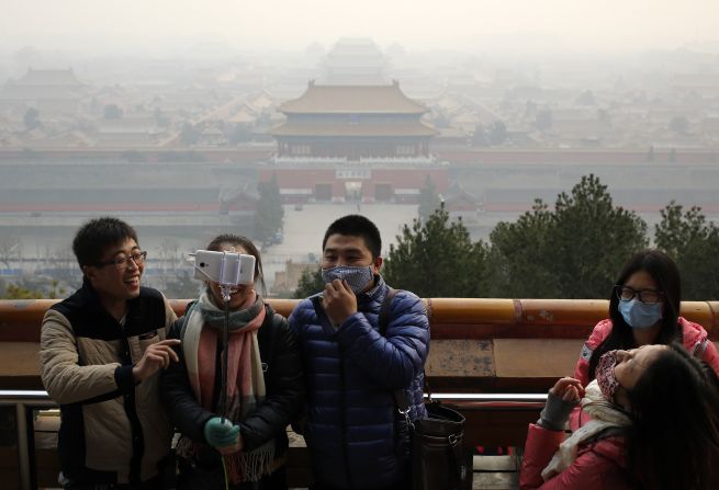 Visitors, some wearing masks to protect themselves from pollutants, share a light moment as they take a selfie at the Jingshan Park on a polluted day in Beijing on December 7, 2015, the day Beijing's city government issued its first red alert for pollution, the highest level of warning.