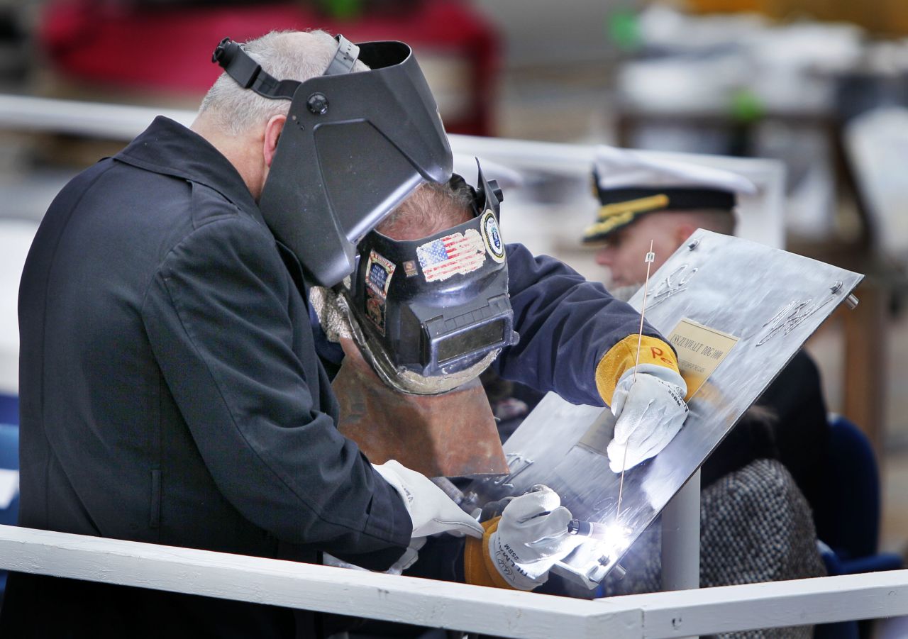 Retired Marine Corps Lt. Col. James G. Zumwalt, left, assists welder Carl Pepin as he inscribes a steel plate at a keel laying ceremony at Bath Iron Works on Thursday, November 17, 2011.