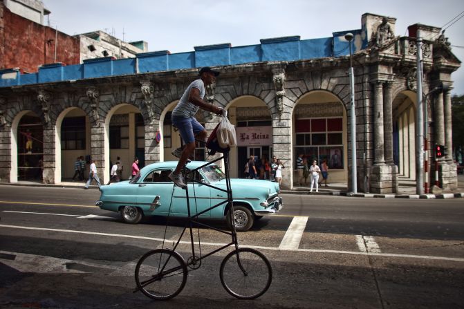 A man rides his modified bicycle past a vintage American car in Havana.