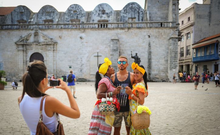 A U.S. tourist poses for a snapshot between two Cubans clad in vibrant attire in Old Havana.