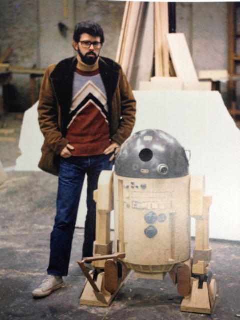 George Lucas stands next to a prototype of R2-D2, the plucky droid that harbored plans for the Death Star. Lucas and Roger Christian played with a variety of models before settling on one that would fit actor Kenny Baker and all the electronics required to move the robot around. It was cramped and hot, and the shoot was testing at times, especially in Tunisia. Christian says R2 often failed to work, and on the opening day of filming struggled to stay upright, resulting in most of the footage being cut from the final version of "A New Hope."