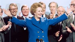British Prime Minister Margaret Thatcher acknowledges applause on Ocotber 13, 1989, at the end of the Conservative Party conference in Blackpool. At left Foreign Secretary John Major and at right Home Secretary John Hurt. (Photo credit: JOHNNY EGGITT/AFP/Getty Images)