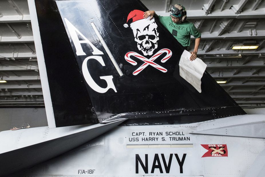 Aviation Structural Mechanic Airman V. Sek, assigned to the "Jolly Rogers" of Strike Fighter Squadron (VFA) 103, applies a Christmas decal to an F/A-18F Super Hornet in the hangar bay of the Nimitz-class aircraft carrier USS Harry S. Truman in December 2015.