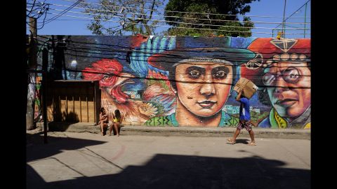 A man carries a package while two young women sit in front of a mural in Rio.