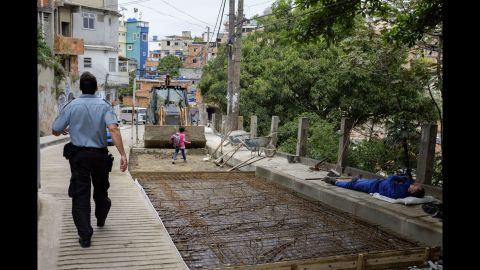 A police officer walks through Cantagalo while a little girl heads past a construction site on her way home from school.