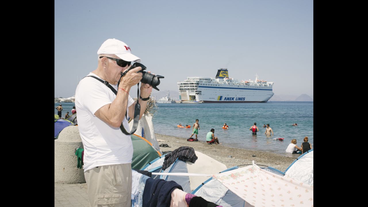 A tourist photographs migrants' tents on the Greek island of Kos. In the background is a ferry that has been converted to a rescue ship for Syrian refugees.