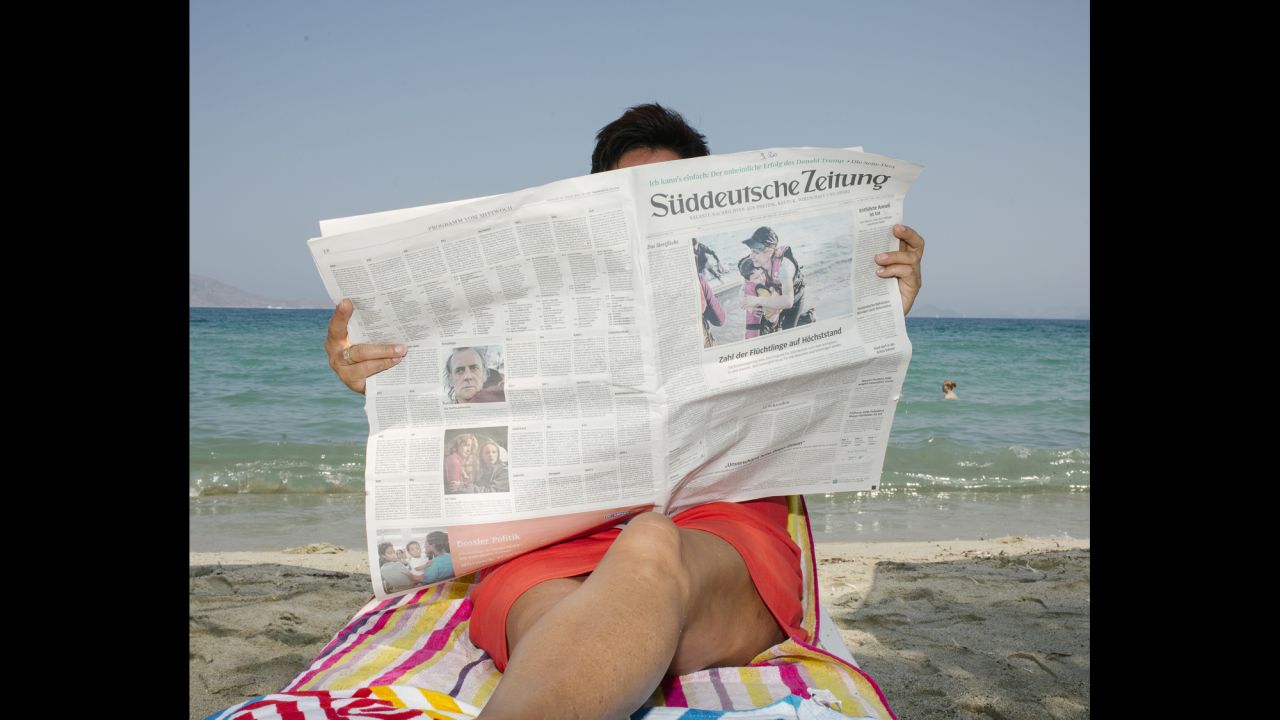 A tourist reads a newspaper on the beach.