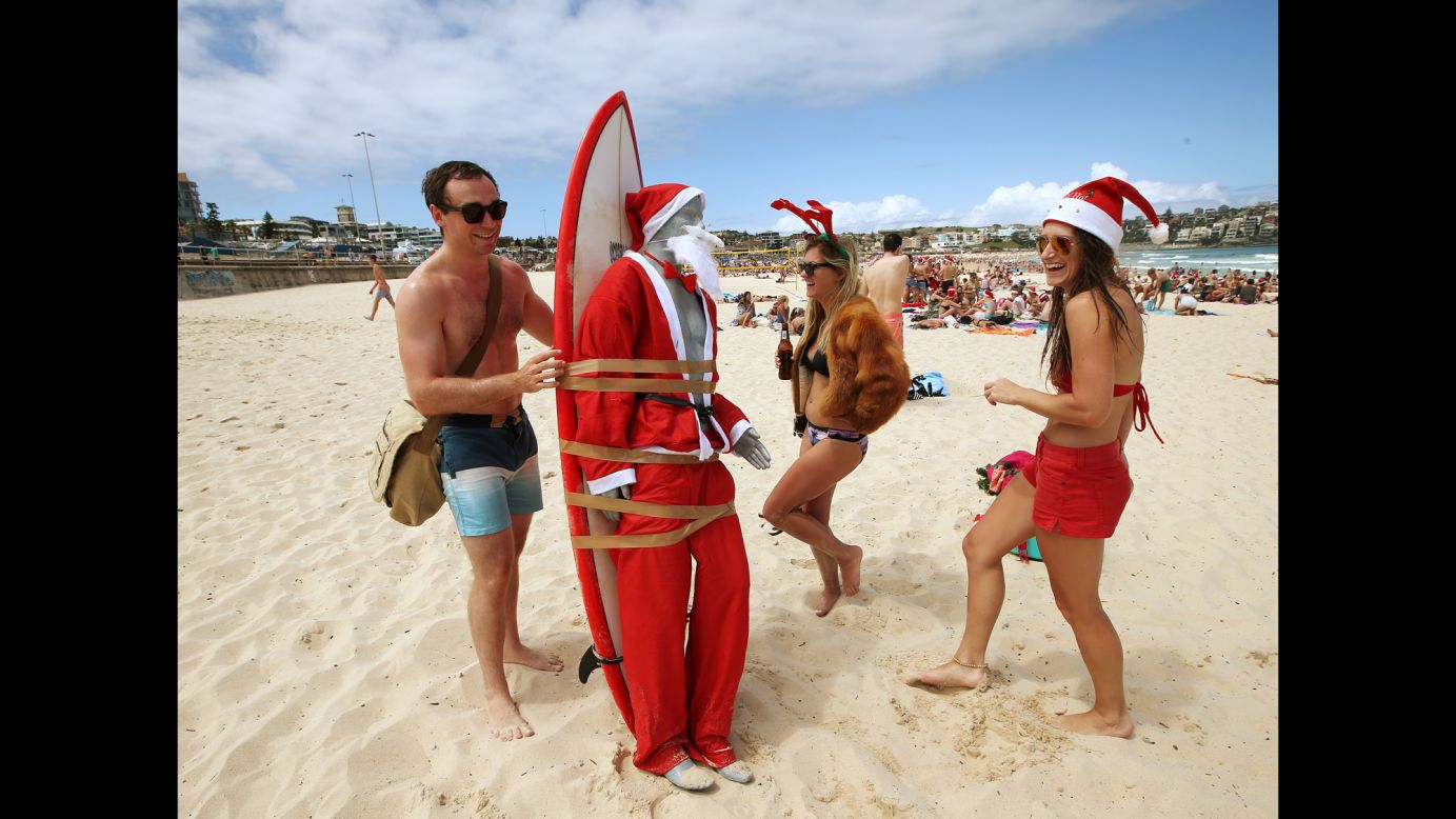 A mannequin in a Santa costume is strapped to a surfboard for easy transport along Bondi Beach as Tom Ray, left, of Britain, Ashley Pronyk of Canada, center, and Helen Maine of Britain celebrate Christmas in Sydney, Australia.