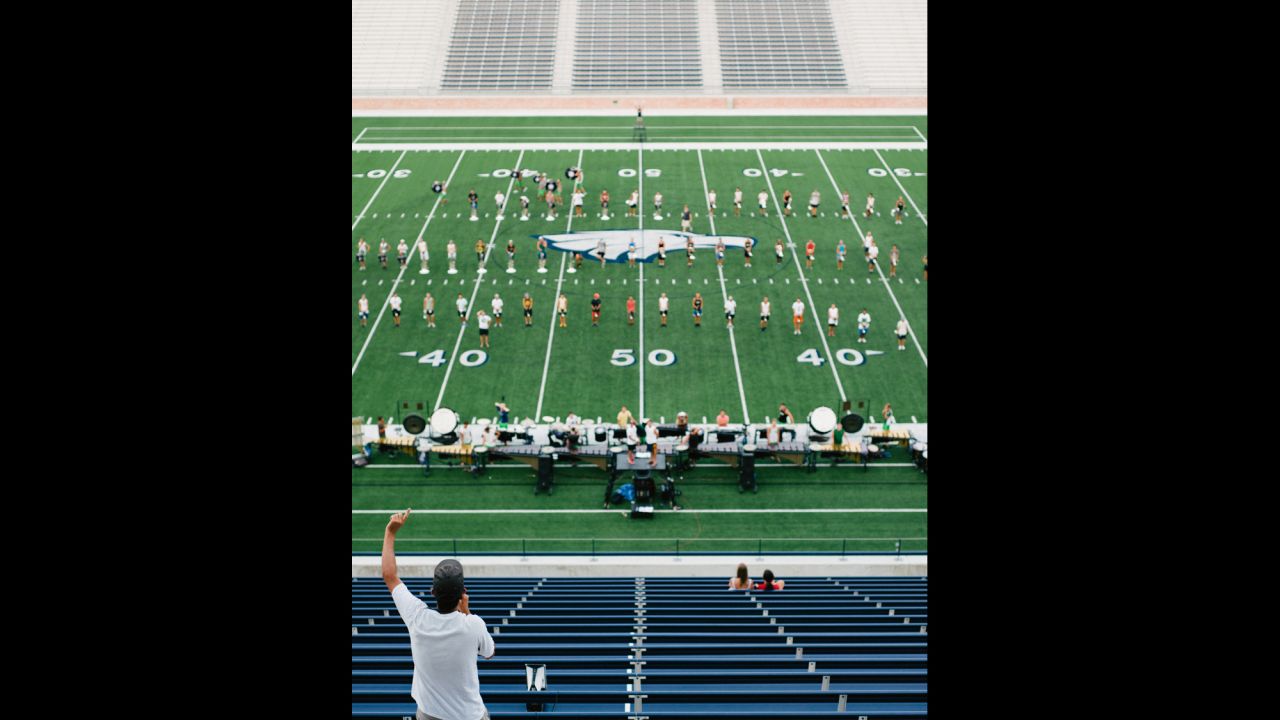A staff member instructs the Cavaliers Drum & Bugle Corps from the upper deck of a stadium.