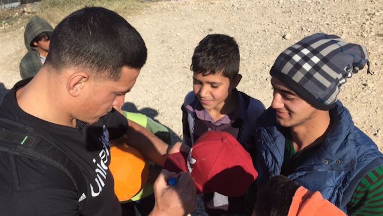 New Zealand rugby star Sonny Bill Williams signs a cap for a Syrian teenager at a refugee camp in Lebanon.