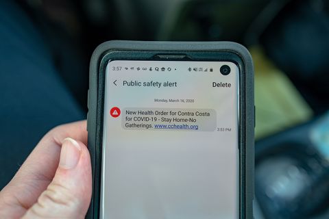 Close-up of hand of a man holding a smartphone displaying an emergency public safety alert text message ordering residents of Contra Costa County, in San Ramon, California into a lockdown and shelter in place during an outbreak of the COVID-19 coronavirus, March 16. 