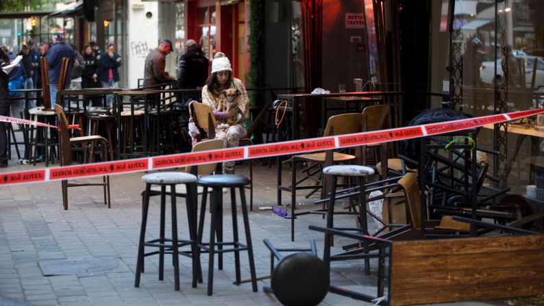 An eyewitness sits with her dog at the scene of <a href="index.php?page=&url=http%3A%2F%2Fwww.cnn.com%2F2016%2F01%2F01%2Fmiddleeast%2Ftel-aviv-pub-shooting%2Findex.html" target="_blank">a shooting in Tel Aviv, Israel,</a> on Friday, January 1. At least two people were killed and four were injured when an unidentified gunman opened fire on a group of people near a pub, authorities said.
