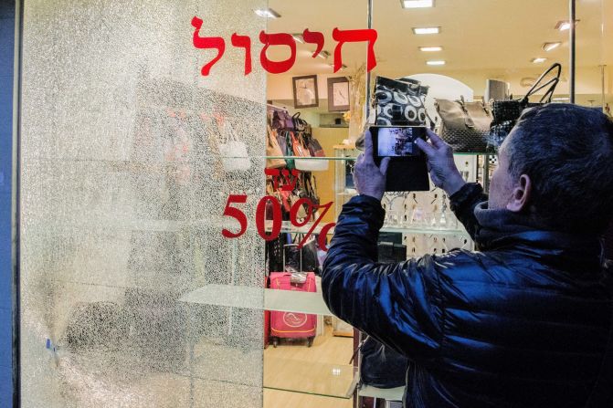 A man takes pictures of a broken shop window.