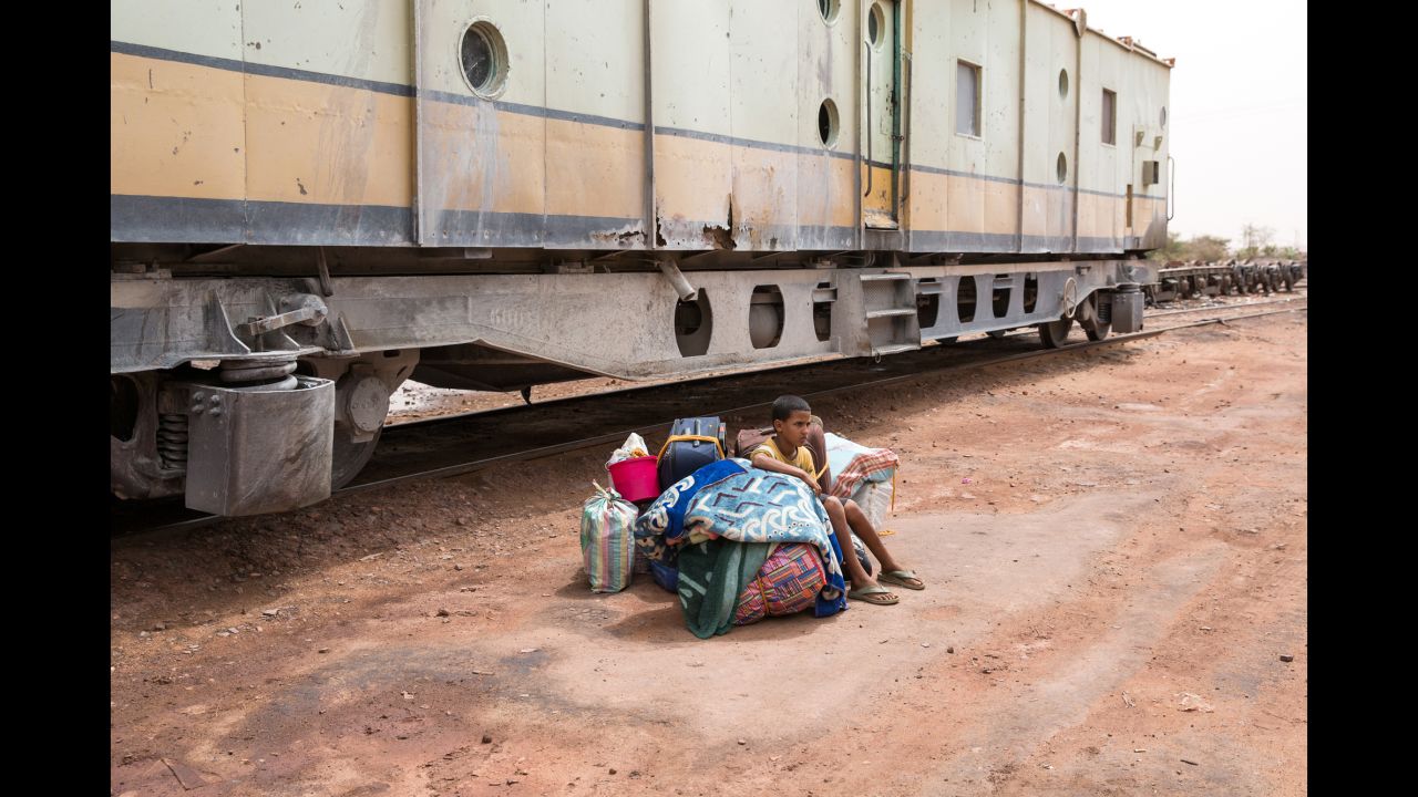 A child sits on luggage as he waits to board a passenger car.