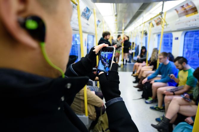 A commuter takes a photo of participants traveling on a London underground train.