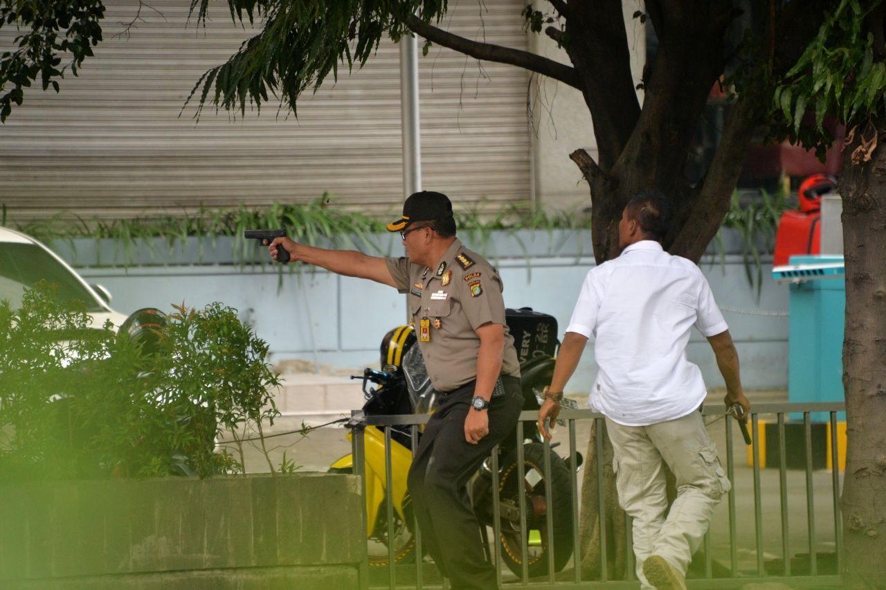 A policeman fires his handgun towards suspects outside a cafe on January 14.
