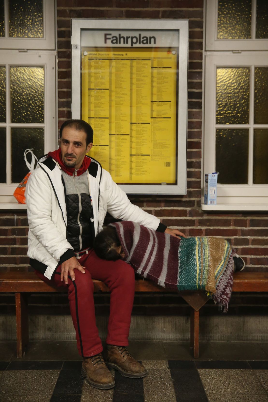 A Syrian hoping for Danish asylum lets his daughter rest in a German train station near Denmark.