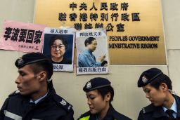 Police walk past missing person notices of Gui Minhai (L) and Yau Wentian (R)