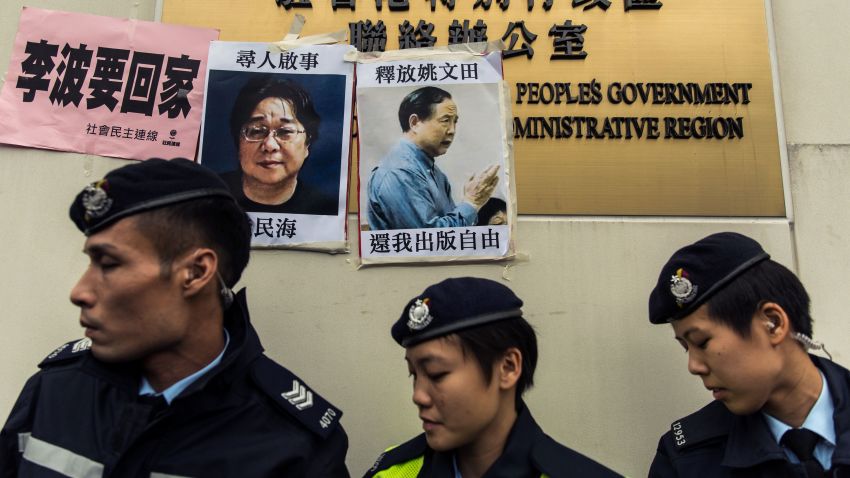 Police walk past missing person notices of Gui Minhai (L), one of five missing booksellers from the Mighty Current publishing house and Yau Wentian (R), a Hong Kong publisher who was last year jailed for 10 years while preparing to release a book critical of Chinese President Xi Jinping, posted on top of the sign of China's Liaison Office in Hong Kong on January 3, 2016. Five missing Hong Kong booksellers were rumoured to have been planning a book about Chinese President Xi Jinping's relationship with a former girlfriend, one of the city's lawmakers said on January 3, as protesters gathered to voice anger over the case.  AFP PHOTO / ANTHONY WALLACE / AFP / ANTHONY WALLACE        (Photo credit should read ANTHONY WALLACE/AFP/Getty Images)