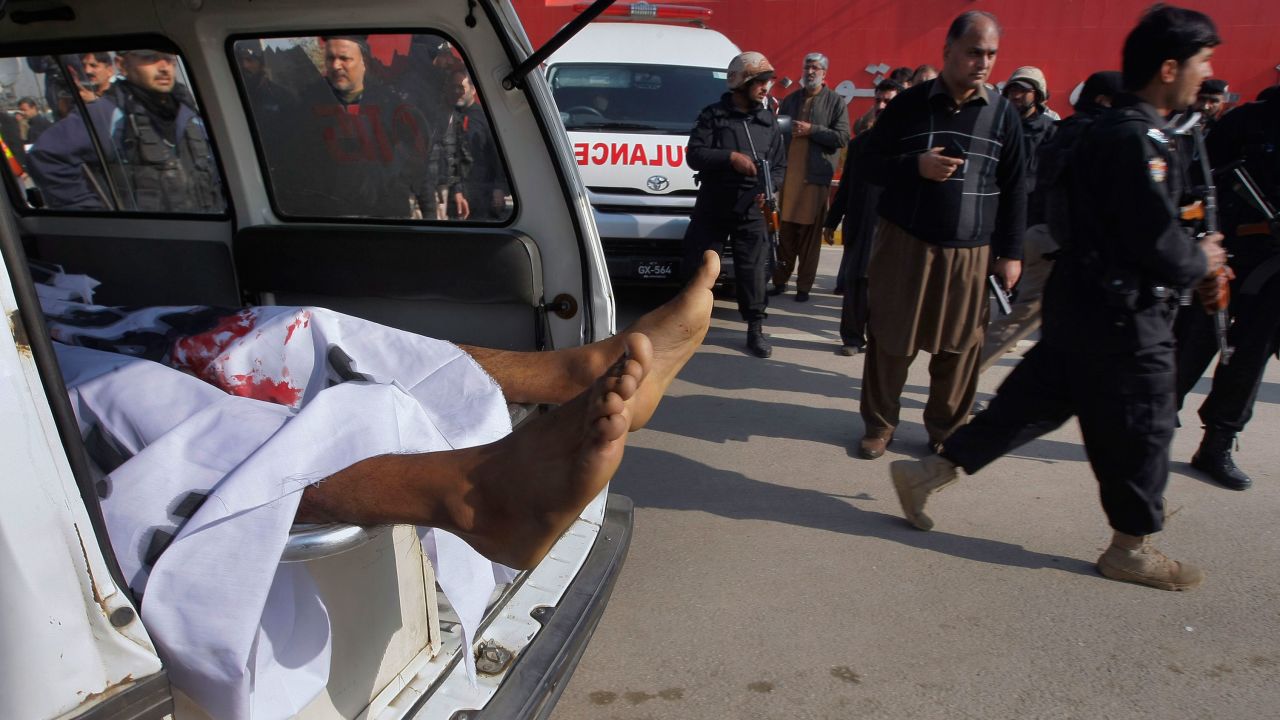 The body of a victim lies in the back of an ambulance while Pakistani troops gather at the main gate of Bacha Khan University.