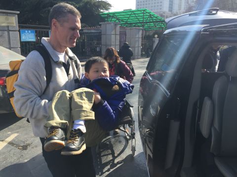 Brian Wilson carries JiaJia to a waiting van. The little boy suffers from spina bifida. Botched surgery left him paralyzed from the waist down. The Wilsons hope further surgeries can help correct some of his problems.