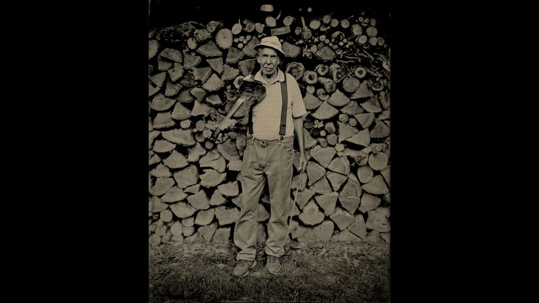 Ralph Roberts holds his fiddle in front of wood he chopped and stacked.
