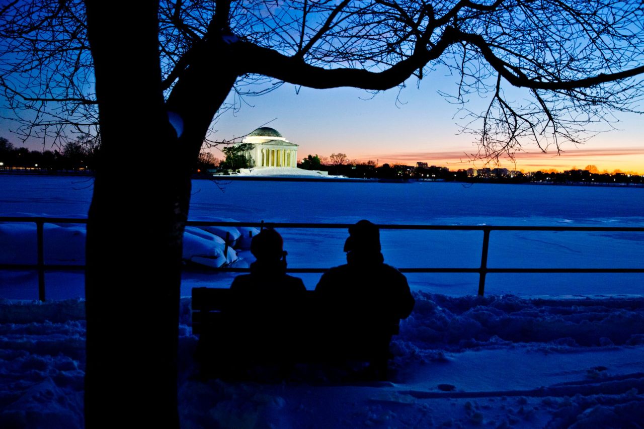 Pirjo Garby, left, and Tom Henry, both of Washington, sit near the Tidal Basin and watch the sunset behind the Jefferson Memorial on Sunday, January 24.