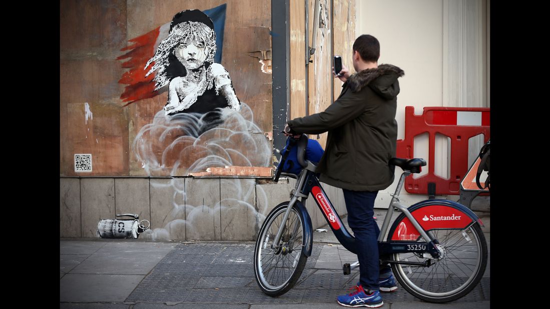 The image, near the French Embassy in London, depicts the character Cosette from the musical Les Miserables as a refugee. It follows reports that French authorities used teargas and rubber bullets to clear sections of the camp earlier this month. An interactive QR code links visitors to a video of the clearance. 