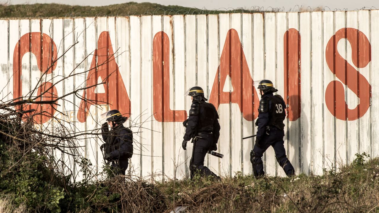 French riot police walk in front of a fence near the A16 motorway near Calais, France.