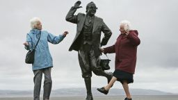 MORCAMBE, UNITED KINGDOM - JUNE 22: Despite inclement weather pensioners raise a happy smile as they perform the famously British dance of comedians Morcambe and Wise next to a statue of Eric Morcambe, at Morcambe Bayon  June 22, 2006, in Morcambe, England.  Confidence & Happiness specialist, Scientist Cliff Arnall from the University of Cardiff has identified June 23, 2006 as being the happiest day of the year. His calculations were based on outdoor activity, nature, social interaction, childhood summers, positive memories, temperature and holidays. (Photo by Christopher Furlong/Getty Images)
