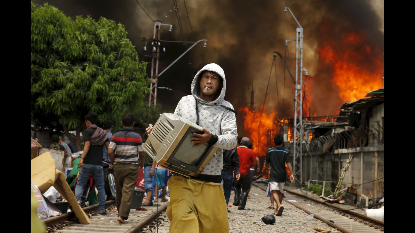 A man carries a television away from a fire in North Jakarta, Indonesia, on Tuesday, January 26. According to local media, the fire destroyed approximately 100 wooden dwellings built along a busy railway line.