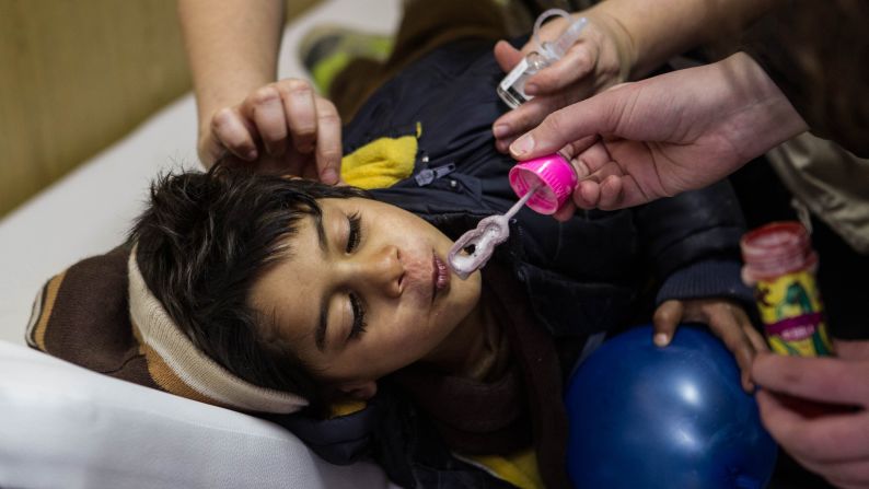 A doctor puts drops in the infected ears of a boy named Farid while volunteers of the ADRA organization distract him at a refugee center in Presevo.