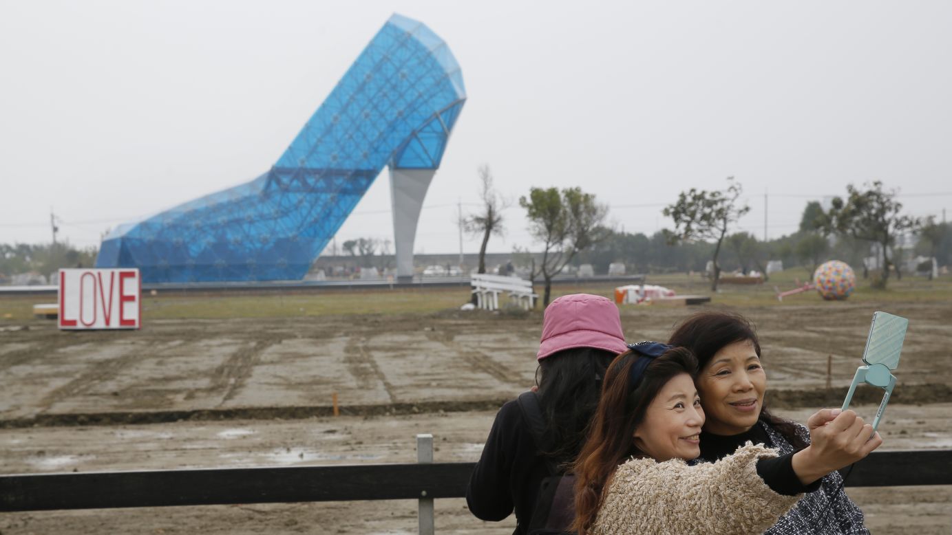 People in Chiayi, Taiwan, take a selfie in front of a glass structure shaped like a high-heeled shoe on Thursday, January 28. The shoe will be a wedding hall when it opens later this month.