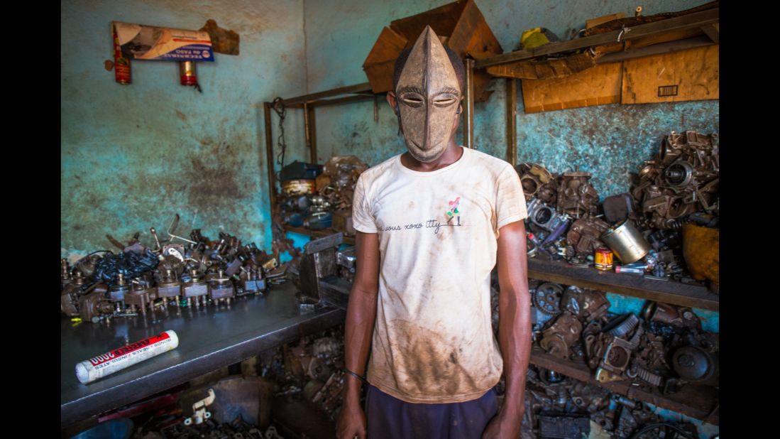 Hoseni, 17, repairs broken cars in Abidjan, Ivory Coast. He is called "Petit," or small, and his monkey mask is from the Hembe ethnic group.