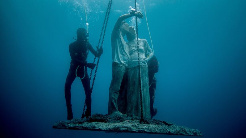 A sculpture named "Content," featuring a faceless couple taking a selfie, is lowered into the sea. 
