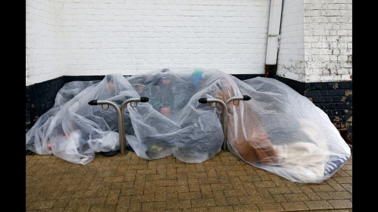 Refugees protect themselves from the rain under a plastic cover in Zeebrugge, Belgium, on Wednesday, February 3.